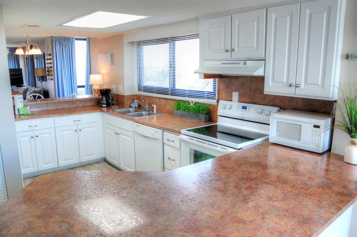 A welcoming kitchen featuring a central island, modern sink, stove, and a window allowing natural light to fill the space. The room is set up for cooking and entertaining, with stainless appliances and ample counter space clearly visible.
