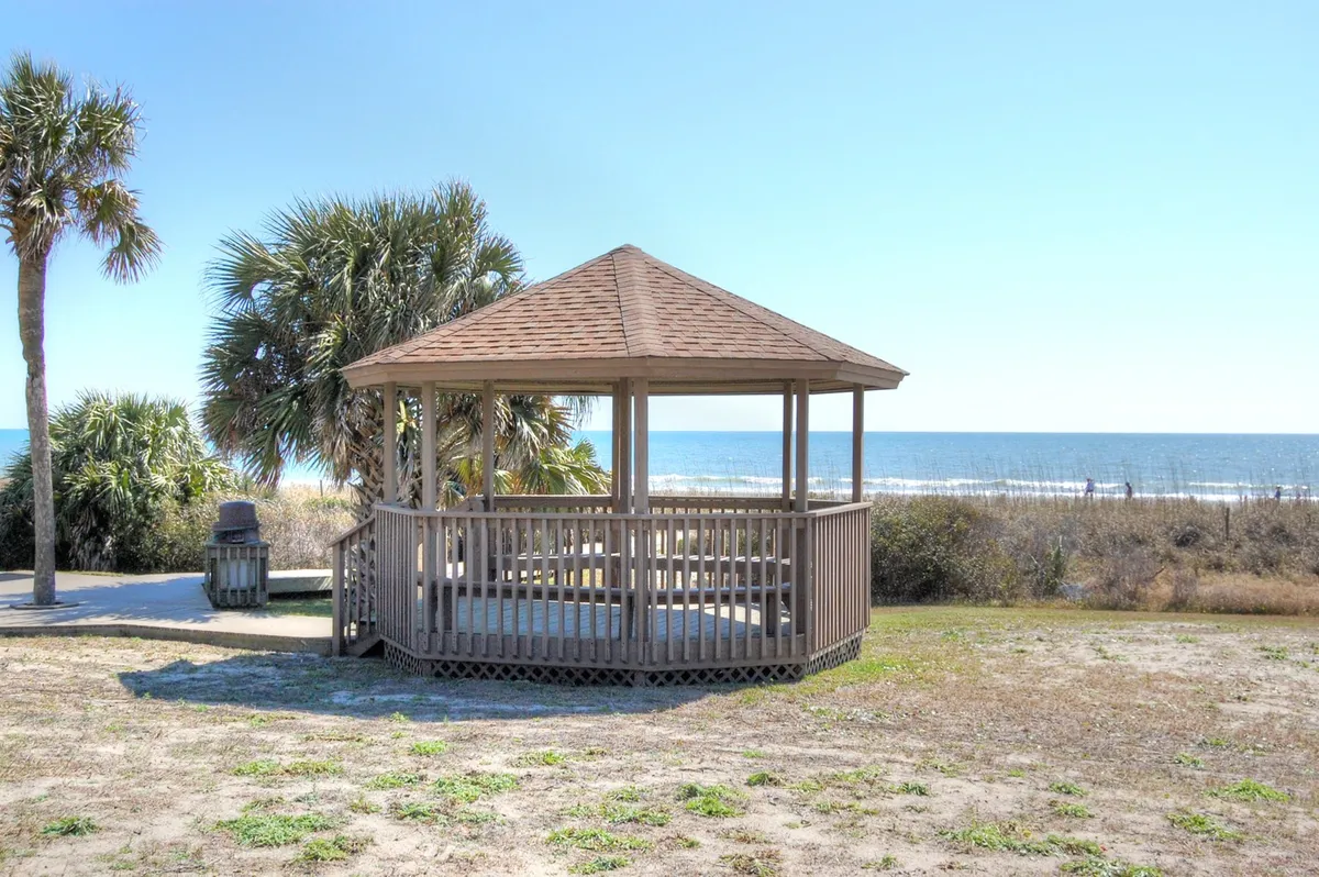 A peaceful beachfront gazebo framed by palm trees and an ocean view. The setting is serene and inviting, evoking relaxation, sunrise strolls, and tranquil moments by the coast.
