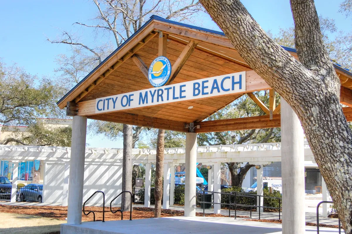 Featuring the 'City of Myrtle Beach' sign, a wooden pavilion, and surrounding trees, this image captures the spirit of local community life. It evokes leisure, social gatherings, and the natural beauty of the area, all under welcoming coastal skies.